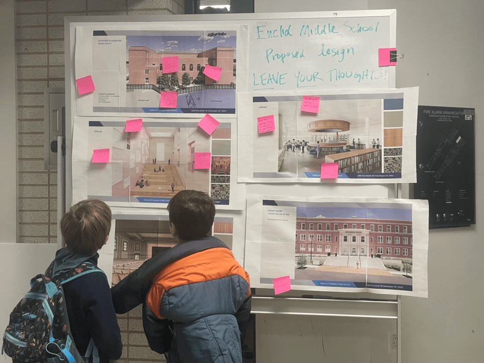 Two children looking at pink post-it notes that show designs of the new middle school on Euclid St. 